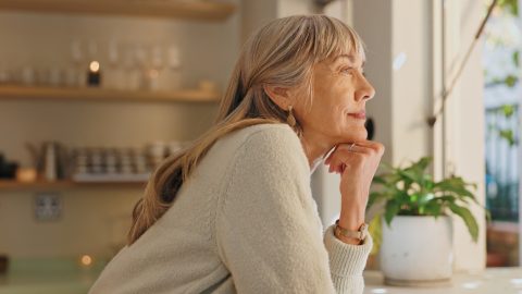 Window, smile and elderly woman with thinking at home for retirement, satisfaction and peace on weekend. Relax, senior person and calm with idea for reflection, mindfulness and good memory in house